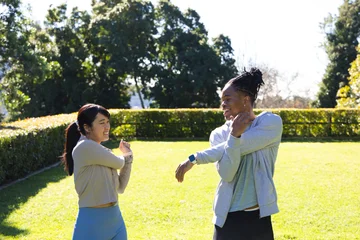 African American man and Asian woman stretching on park lawn near hedge in sportswear, smartwatch © WavebreakMediaMicro
