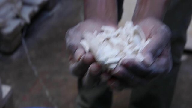 Hands holding dried cassava chips over a bucket