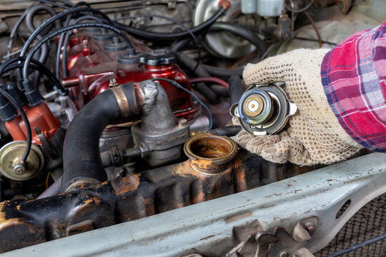 Horizontal stock photo of mechanic holding removed radiator cap in car engine bay