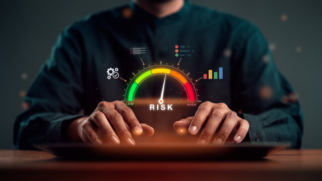 Risk management and business risk assessment concept. Businessman hands on desk under glowing risk meter gauge from green to red with needle, gear and chart icons.