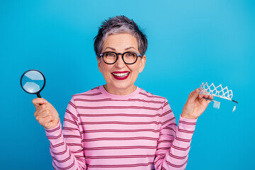 Smiling mature woman holding magnifying glass and tiara, playful confident senior celebrating fun and self-discovery © deagreez