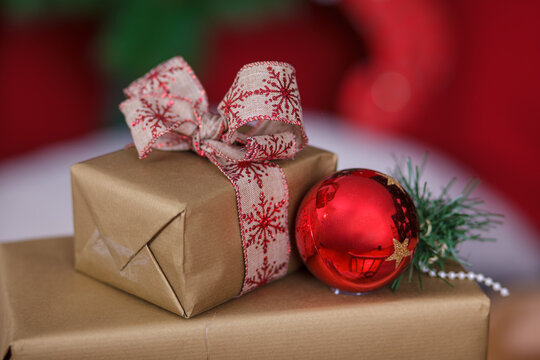 Golden Christmas Gift Boxes Wrapped with Ribbon Bow and Red Bauble on Blurred Tree Background for Holiday Celebration