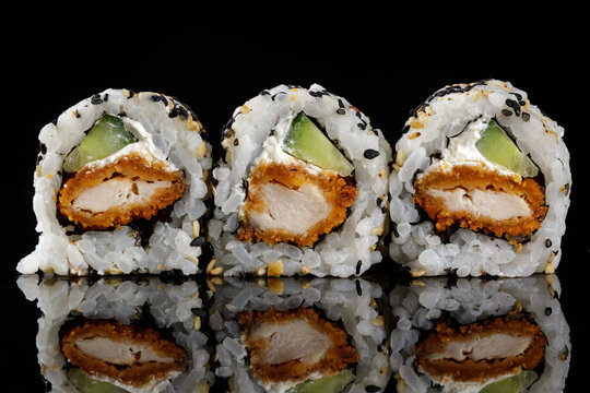 Three crispy chicken uramaki sushi rolls with cream cheese,cucumber and sesame seeds on black reflective background. Gourmet Japanese restaurant menu. Japanese cuisine