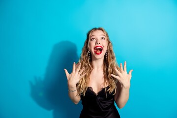 Plakat Excited young woman in black dress celebrating with joyful expression against bright blue background