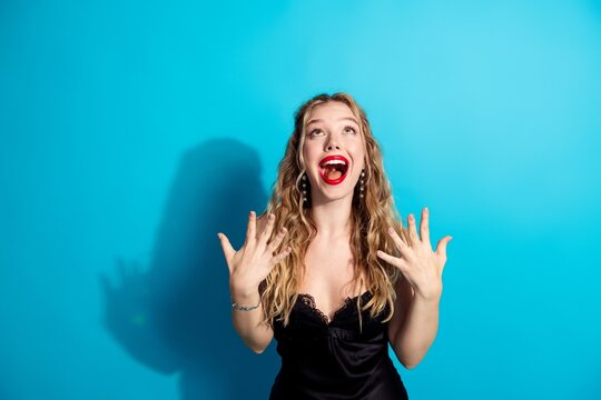 Excited young woman in black dress celebrating with joyful expression against bright blue background