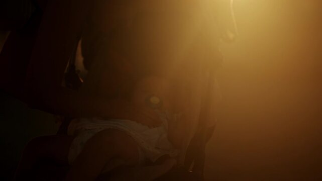 Silhouette of a mother leaning over a stroller to tend to her baby with a pacifier in hazy golden sunset backlight, French Riviera, France.