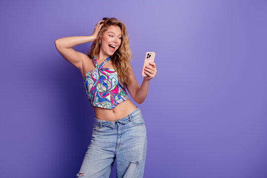 Happy young woman taking a selfie with smartphone against purple background wearing colorful halter top and ripped jeans, casual summer lifestyle and joyful expression