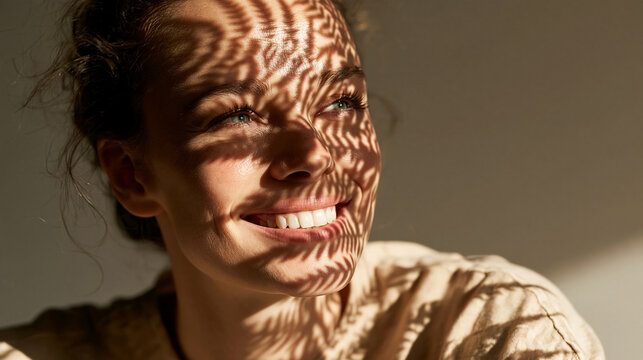 Smiling young woman experiencing warm sunlight casting beautiful leaf shadows across her face indoors