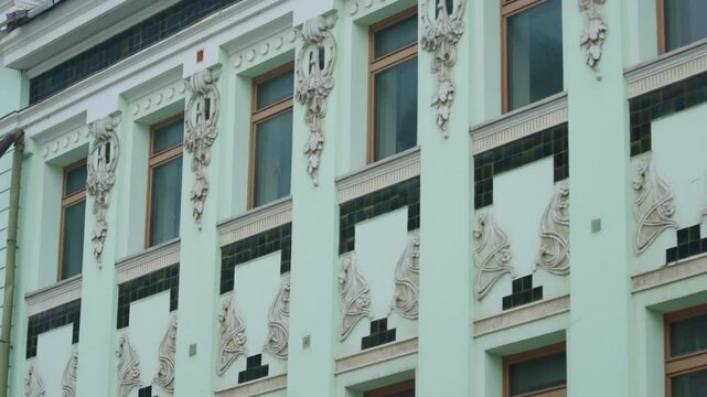 Ornate stucco decorations frame large glass windows on pastel facade. Historic urban architecture reflects sophisticated artistic charm