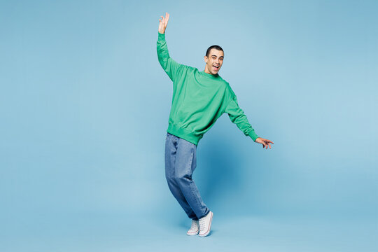Full body young middle eastern man he wear green shirt casual clothes standing on toes dancing lean back have fun spread hands isolated on plain pastel light blue cyan background. Lifestyle concept