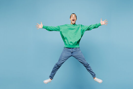 Full body young middle eastern man wear green shirt casual clothes jump high with outstretched hands legs look camera isolated on plain pastel light blue background studio portrait. Lifestyle concept.