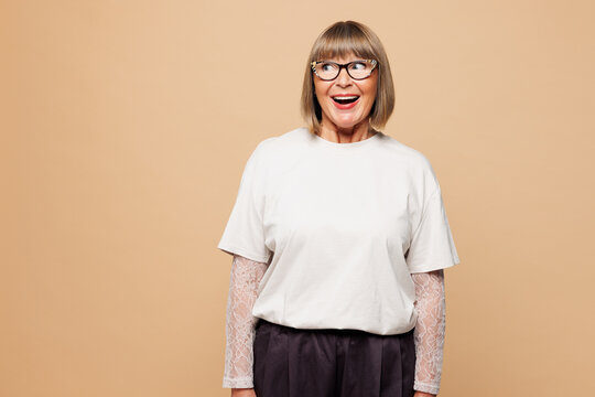 Elderly shocked surprised amazed cool blonde woman 50s years old she wear white shirt casual clothes look aside on empty blank area isolated on plain pastel light beige background. Lifestyle concept.