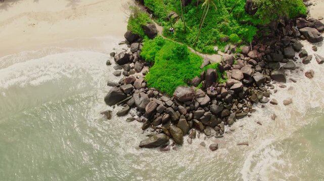 Aerial view of Vagator Beach with rocky cliffs, lush greenery, and waves crashing against the shore in Anjuna, Goa, India.