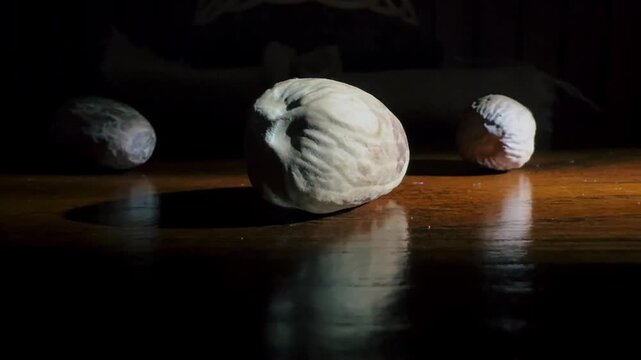 Macro zoom in shot of raw whole nutmeg seeds showing rich organic texture on a glossy teak wood table with warm shadow reflection