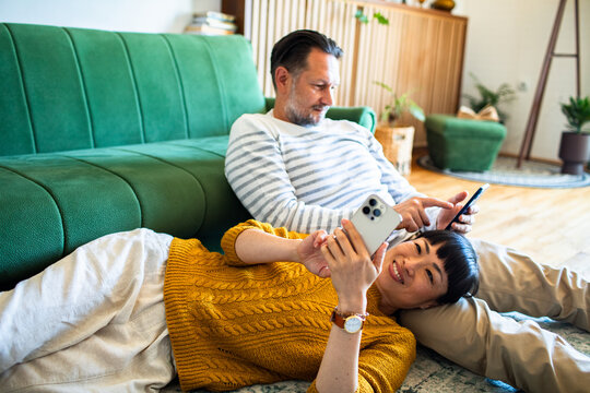 Couple lounging on the living room floor using smartphones