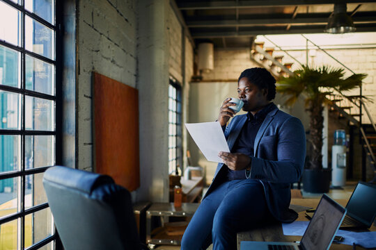 Businessman drinking coffee and reading a document in a loft office