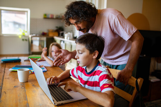 Parent helping boy with homework on laptop at kitchen table