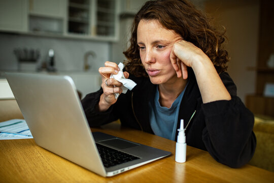 Sick woman with tissue using laptop at home