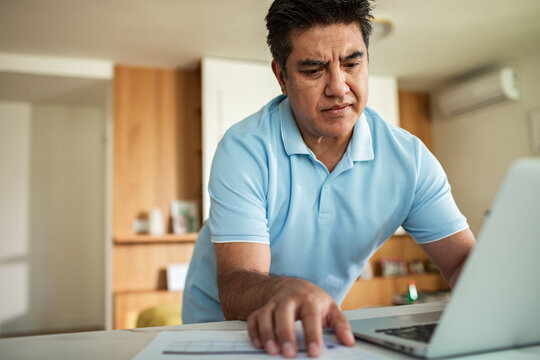 Man reviewing paperwork while using laptop at home