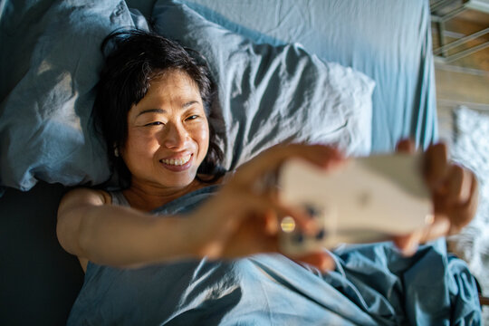 Smiling woman taking selfie in bed at home