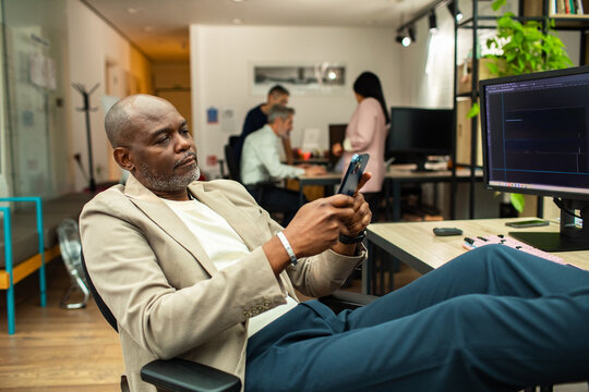 Mature man leaning back using smartphone at office desk