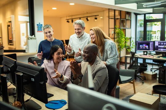 Coworkers applaud while looking at a computer screen in the office