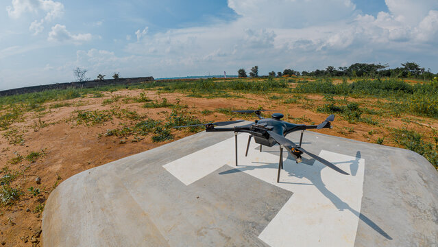 View of a professional drone resting on a concrete helipad in a dry, open field under a bright blue sky in India.