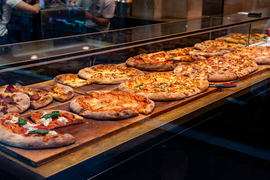 Fresh Italian pizzas displayed behind glass in a traditional pizzeria