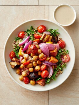 Hearty grain bowl topped with roasted vegetables and chickpeas is served with a creamy dressing.