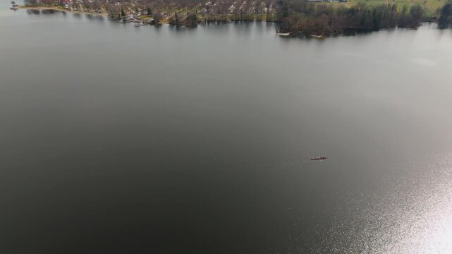 Scenic aerial video of Waginger See in the Traunstein district of Bavaria, Germany. A lone fisherman in a small boat crosses the calm freshwater lake beneath a hazy spring sky.