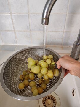 Woman carefully washing fresh grapes in a kitchen sink, removing dirt and potential contaminants for safer, cleaner eating. 