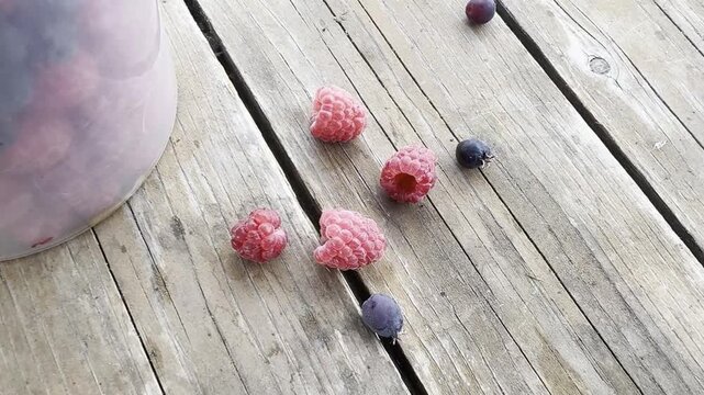 Fresh raspberry and serviceberry lie on rustic wood as the camera slides toward a full berry bowl in natural light, for harvest, nutrition, organic food, rural life and seasonal produce. 4K video.