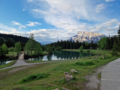 View of Two Jack Lake with a wooden bridge, surrounding coniferous forest, and a mountain peak under a blue sky in Banff National Park, Improvement District No. 9, Alberta, Canada.