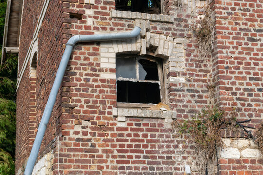 Detailed view of broken window glass, weathered brickwork, decorative masonry and metal drainpipe on the former Relais de poste in Marle, Aisne, France. The historic postal station has a protected fac