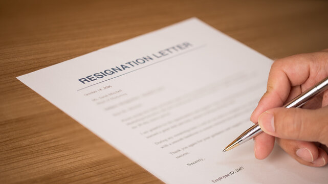 Person hand signing a resignation letter document on a wooden desk. Career change, job quitting, employment contract termination, and professional corporate office transition concept