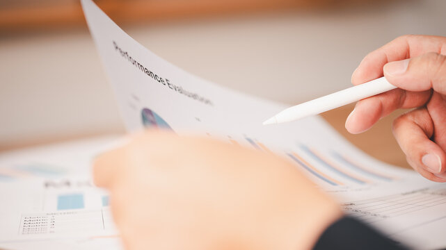Close-up person holding stylus pen reviewing performance evaluation report document data charts. Concept corporate business review employee assessment analysis planning strategy success management