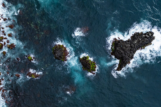 Aerial top down view of Atlantic waves breaking around volcanic rocks. Dynamic ocean surface and sea foam texture fit coastal nature