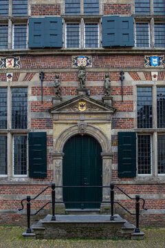 View of the historic brick facade of the Naarden-Vesting building, featuring an ornate stone doorway, green shutters, and decorative statues in Naarden, Noord-Holland, Netherlands.