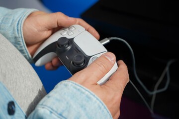 Close-up of hands using a wired game controller against a dark blue background. Selective focus highlights the controller and fingers during video gaming and digital entertainment. © Dr. CraftLab
