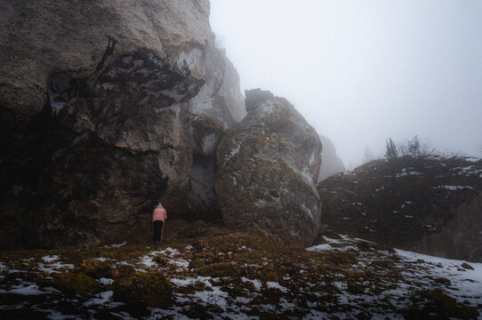 Winter Landscape: Person in Pink Jacket by Snow-Covered Rock Formation in Mist - Nature's Grand Sculptures
