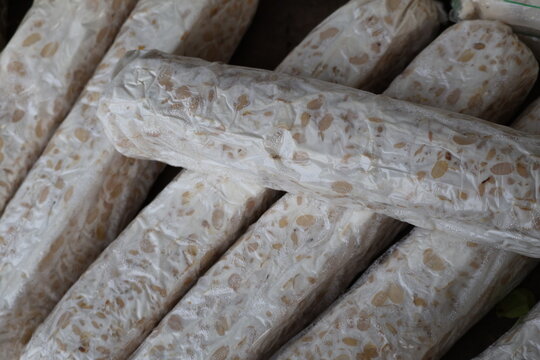 Fresh raw tempeh wrapped in transparent plastic packaging, traditional Indonesian fermented soybean food.