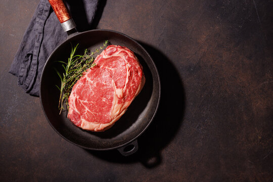 Raw beef ribeye in skillet on dark surface
