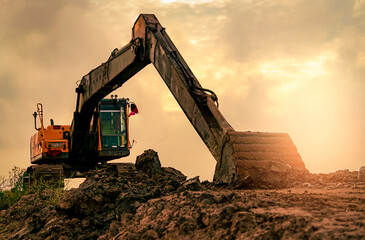 Tracked excavator parked on uneven soil at a construction site at sunset, with an extended hydraulic arm and a dirt covered bucket resting on the ground after digging, heavy equipment for earthmoving. © Fahroni