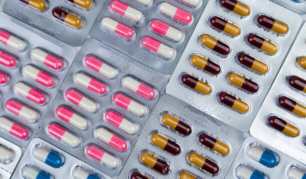 Antibiotic capsules in silver blister packs, pink and white pills beside yellow and burgundy capsules with blue and white medicine, pharmaceutical packaging for pharmacy and global healthcare.