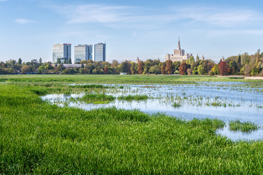 View of King Mihai I Park with lush green grass, a calm lake, and a distant skyline featuring modern skyscrapers and the historic Casa Presei Libere building in Bucharest, Bucharest, Romania.