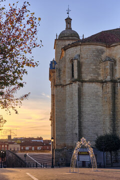View of the historic Iglesia de Santiago with its stone facade in golden hour light, featuring a decorative arch and autumn foliage in Cigales, Castilla y Leon, Spain.