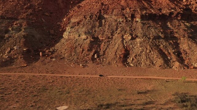 Aerial view of rugged red rock cliffs and dirt road beside river