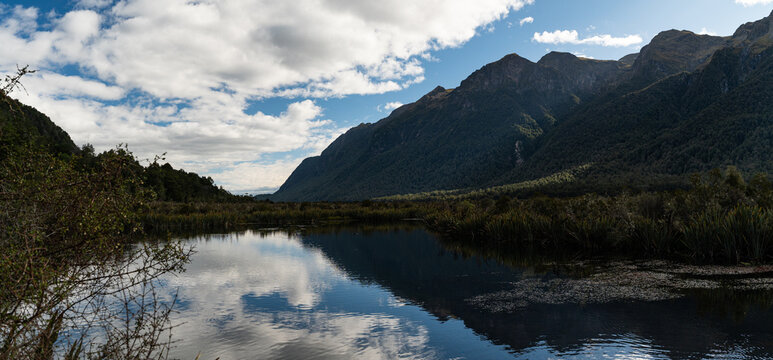 View of Lake Howden on the Routeburn Track, featuring calm reflective waters, lush surrounding forest, and dramatic mountain peaks in Southland Region, New Zealand.