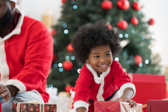 African American father celebrates Christmas and give Christmas gift box to little son in festive living room. Happy cute African American little boy with Chirstmas gift box