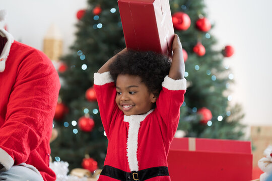 African American father celebrates Christmas and give Christmas gift box to little son in festive living room. Happy cute African American little boy with Chirstmas gift box